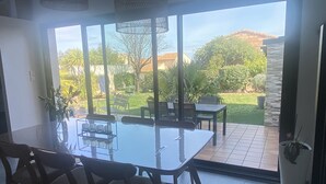 A dining area with a glass table and chairs, a view of a garden and hills outside. - Villa Tout Confort Entre MER ET Etang (Sète)