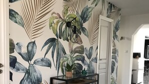 A hallway with a tropical leaf pattern on the walls, a glass-top console table, and a door leading to another room. - Villa Tout Confort Entre MER ET Etang (Sète)
