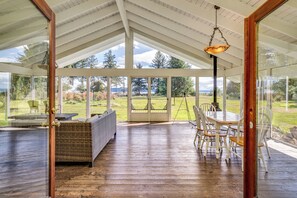 Eine geräumige, überdachte Veranda mit Essbereich, einem Rattangeflechtsofa und Blick auf einen üppigen Garten und Berge.