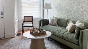 A living room with a green sofa, a round coffee table, a wicker chair, and a patterned rug. - Beautiful 4bd, 2.5ba Lancaster Center City Townhome (Lancaster)