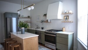 A modern kitchen with a central island, stainless steel appliances, wooden stools, and decorative items on shelves. - Beautiful 4bd, 2.5ba Lancaster Center City Townhome (Lancaster)