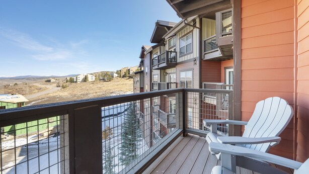 A balcony with a view of a hilly landscape, a white Adirondack chair, and a building with a brown exterior. - Pool & Pedals Biking Base at Granby Ranch (Granby)
