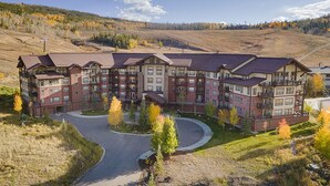 A multi-story hotel with a central courtyard, surrounded by a hilly landscape with autumn foliage. - Pool & Pedals Biking Base at Granby Ranch (Granby)