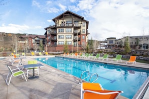 A swimming pool with lounge chairs and a building with multiple balconies in the background. - Pool & Pedals Biking Base at Granby Ranch (Granby)