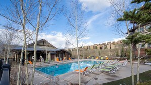 A swimming pool with lounge chairs, a building with a sloped roof, and a clear sky. - Pool & Pedals Biking Base at Granby Ranch (Granby)