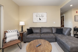 A living room with a gray sectional sofa, a wooden coffee table, a lamp, and a sign on the wall. - Pool & Pedals Biking Base at Granby Ranch (Granby)