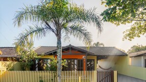 A two-story house with a tiled roof, a wooden fence, and a palm tree in front. - House with pool Guaratuba-Barra do Saí - 100 m from the beach (Guaratuba)