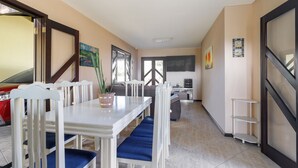 A dining area with a white table and blue chairs, a red car parked outside, and a kitchen in the background. - House with pool Guaratuba-Barra do Saí - 100 m from the beach (Guaratuba)
