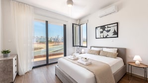 Une chambre d’hôtel moderne dotée d’un grand lit, d’un balcon avec vue, d’une télévision à écran plat et d’une petite table avec une lampe.