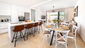 Une cuisine moderne avec des meubles blancs, un îlot central doté de tabourets et un coin repas comprenant une table ronde et des chaises.