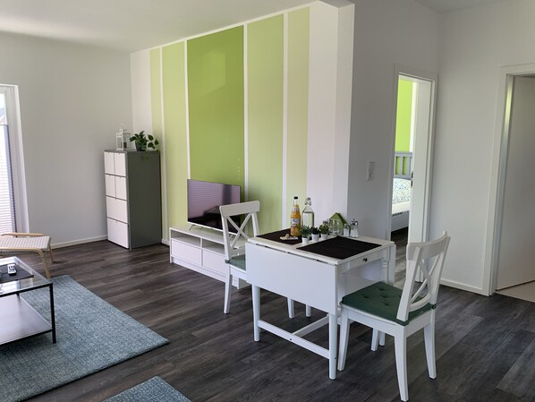 Une pièce moderne et bien éclairée, avec un bureau blanc, deux chaises, une petite table et un meuble de rangement.