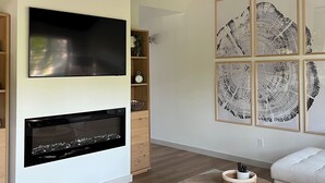 Een moderne woonkamer met een flatscreen televisie, een open haard, een plafondventilator en kunst aan de wand.
