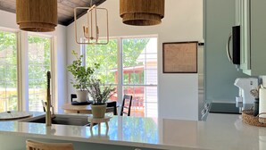 Een keuken met houten barstoelen, een groot eiland, hangende rieten lampen en uitzicht op de omgeving.