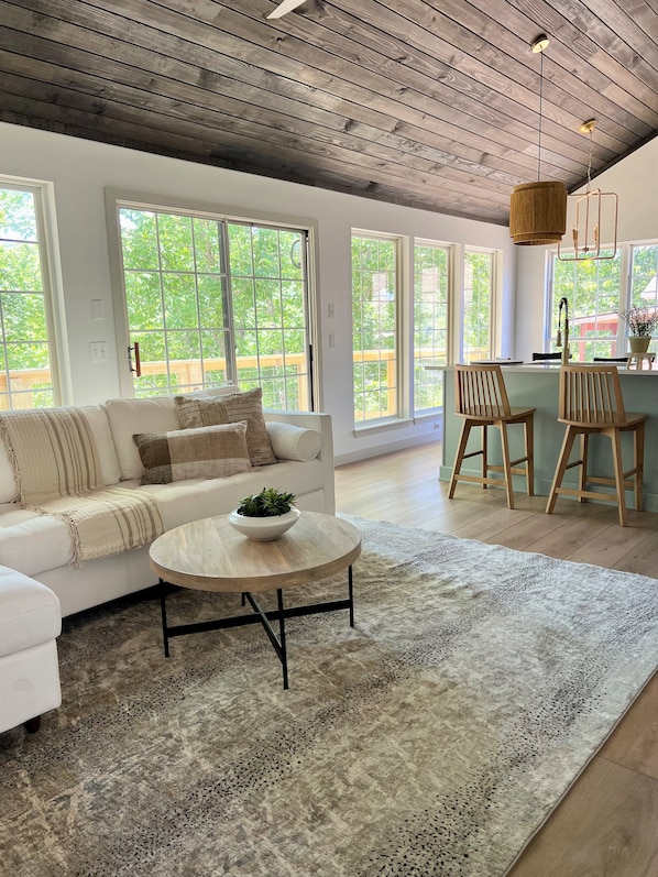 A spacious living area with a white sofa, a round coffee table, and a large window offering a view of greenery.