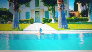 A pool area with a clear view of a building with a green door and windows, surrounded by trees and a well-maintained lawn. - Villa near beach, golf course, verdon gorges (Trans-en-Provence)