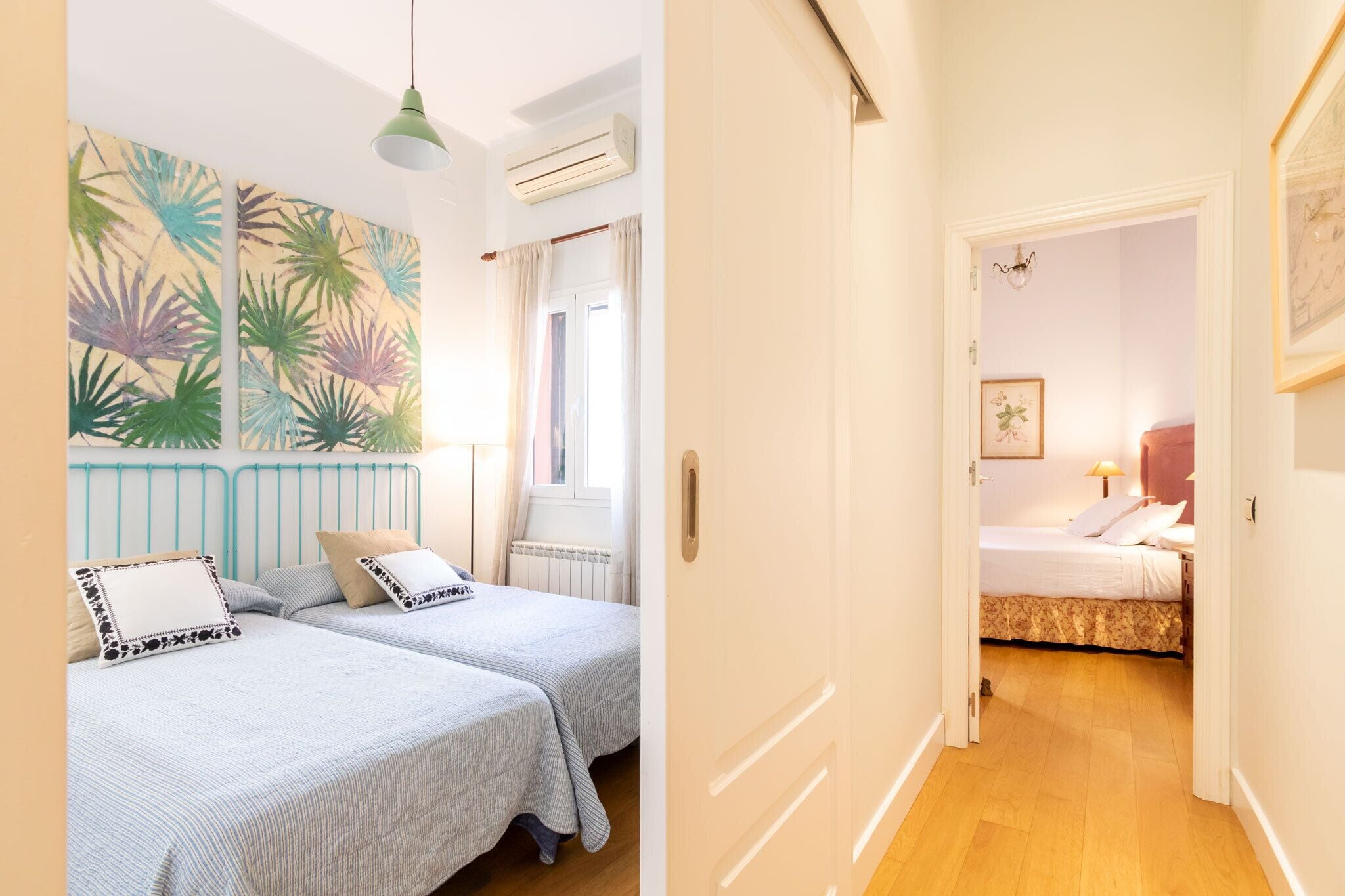A room with two beds, a large tropical plant wall, and a door leading to another room.