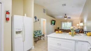 Una cocina con refrigerador, una zona de comedor con mesa y sillas, y un ventanal con cortinas.