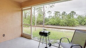 Un balcón con una parrilla, una silla y vistas al verdor.