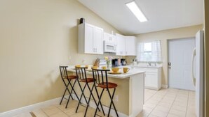 Cocina compacta con armarios blancos, microondas y una pequeña isla con taburetes.