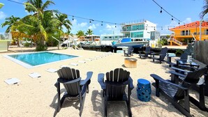 A poolside area with Adirondack chairs, a small round table, and a boat docked nearby. - Casa Azul, Key Largo, Home w Private Pool & Dock (Key Largo)