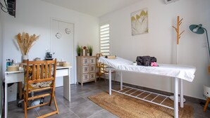 A clean, well-lit room with a desk, chair, and a small table with a white tablecloth. There is a decorative plant, a wall-mounted air conditioner, and a framed artwork on the wall. - Hôtel Guadeloupe Palm Suites (Saint-François)