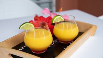 Dos vasos de jugo de naranja con rodajas de lima sobre una bandeja de madera.