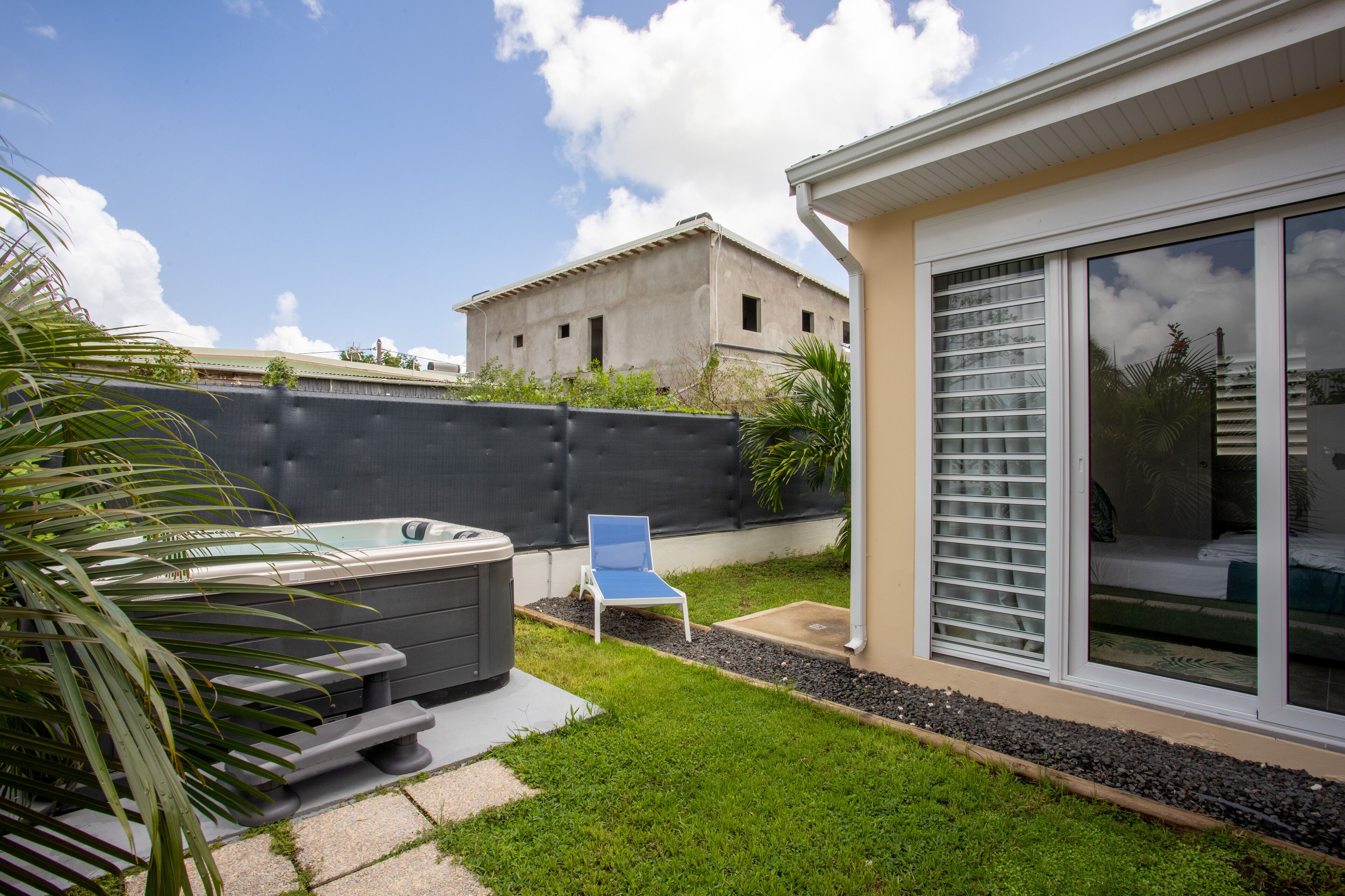 Een modern huis met een jacuzzi, een patio stoel en een grote glazen schuifdeur die leidt naar een slaapkamer.