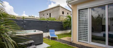 A modern house with a hot tub, a patio chair, and a large sliding glass door leading to a bedroom.