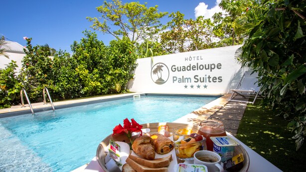 A poolside breakfast tray with croissants, fruit, yogurt, and juice at the HOTEL Guadeloupe Palm Suites. - Hôtel Guadeloupe Palm Suites (Saint-François)