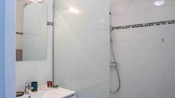 Une salle de bain moderne avec une douche à parois de verre, un lavabo blanc avec un miroir et un sol de douche carrelé.