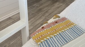 Quarto com cama, um pequeno armário, uma cesta de vime e piso de madeira.