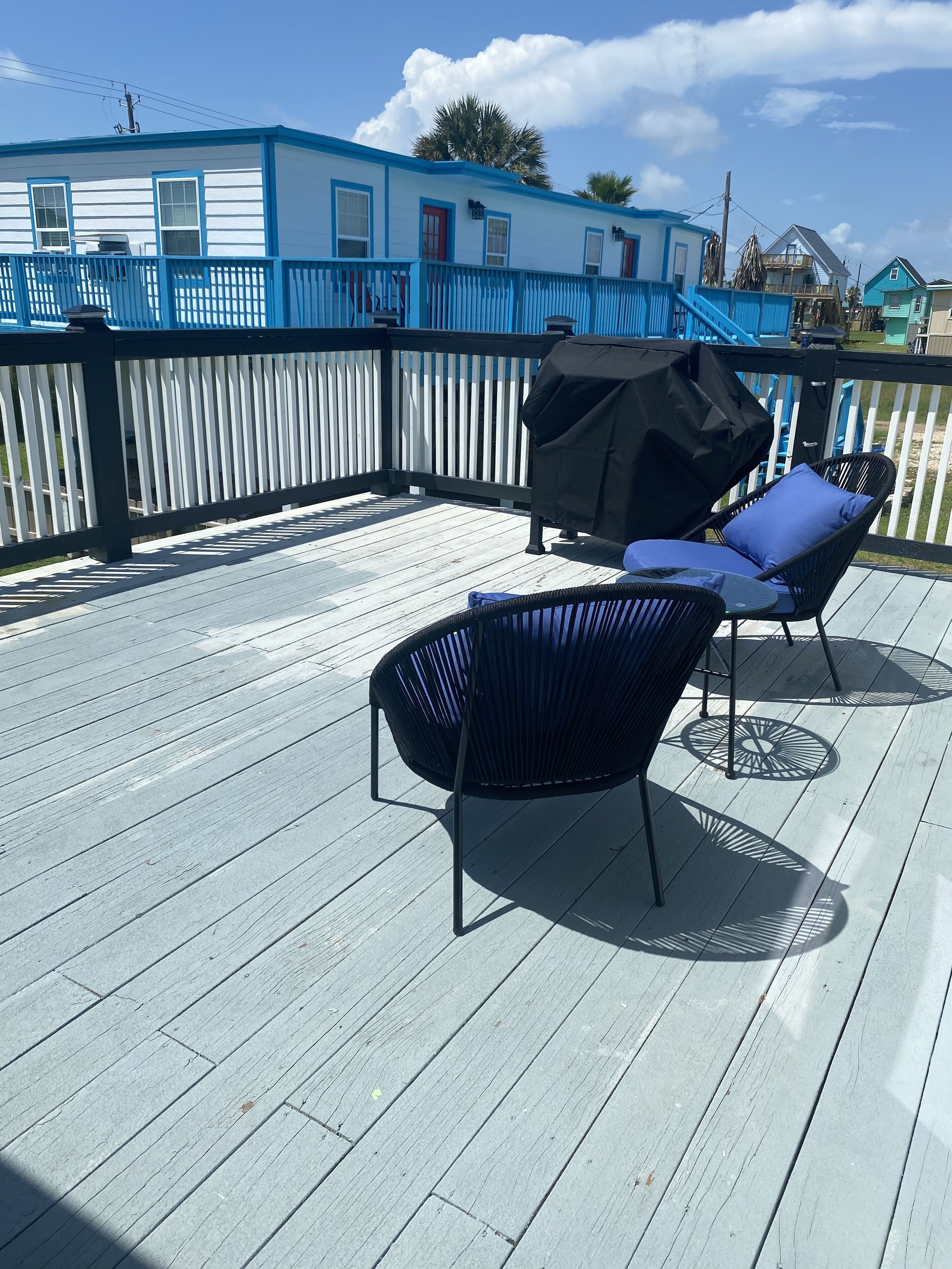 A wooden deck with two black lounge chairs and a barbecue grill.