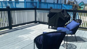 Um deck de madeira com duas cadeiras de lounge pretas e uma churrasqueira.