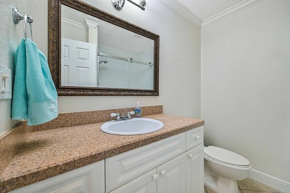 A bathroom with a granite countertop, a white sink, a mirror, a towel rack, and a toilet.