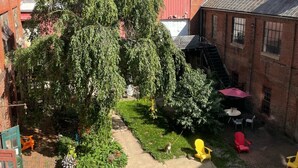 En innergård med ett stort träd, byggnader i tegel och utomhusmöbler.