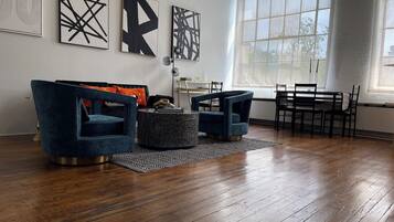 A modern living room with a dark blue sofa, two armchairs, a coffee table, and a dining area with a table and chairs.