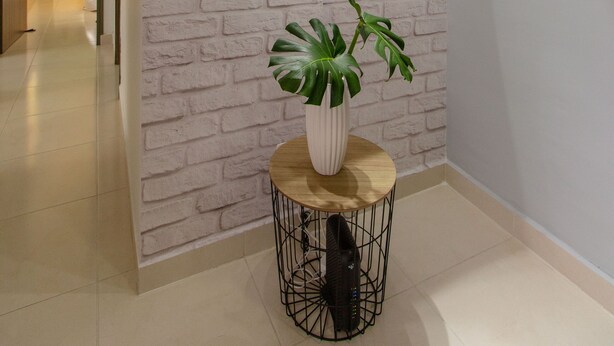 Un pasillo con pared de ladrillo blanco, un espejo redondo, una planta en maceta y un letrero que dice 'hi'.
