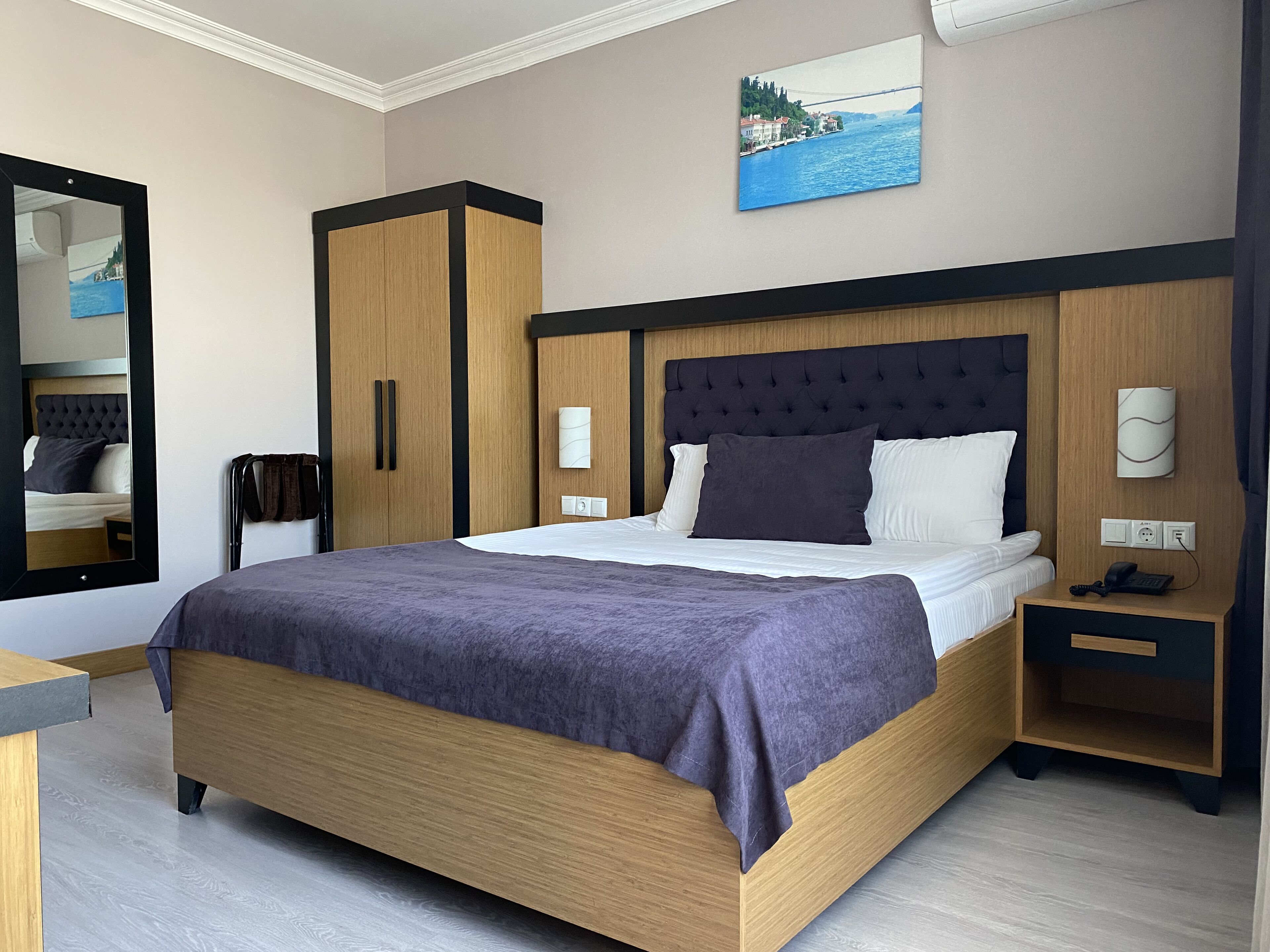 Ein modernes Hotelzimmer mit einem großen Bett, einem Schrank, einem Nachttisch mit Telefon und einem Gemälde an der Wand.
