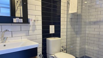 A modern bathroom with a white sink, black and white tiled walls, a toilet, and a glass shower enclosure.