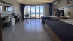 Hotelkamer met een bed, bureau, stoel, televisie en een groot raam met uitzicht op zee.