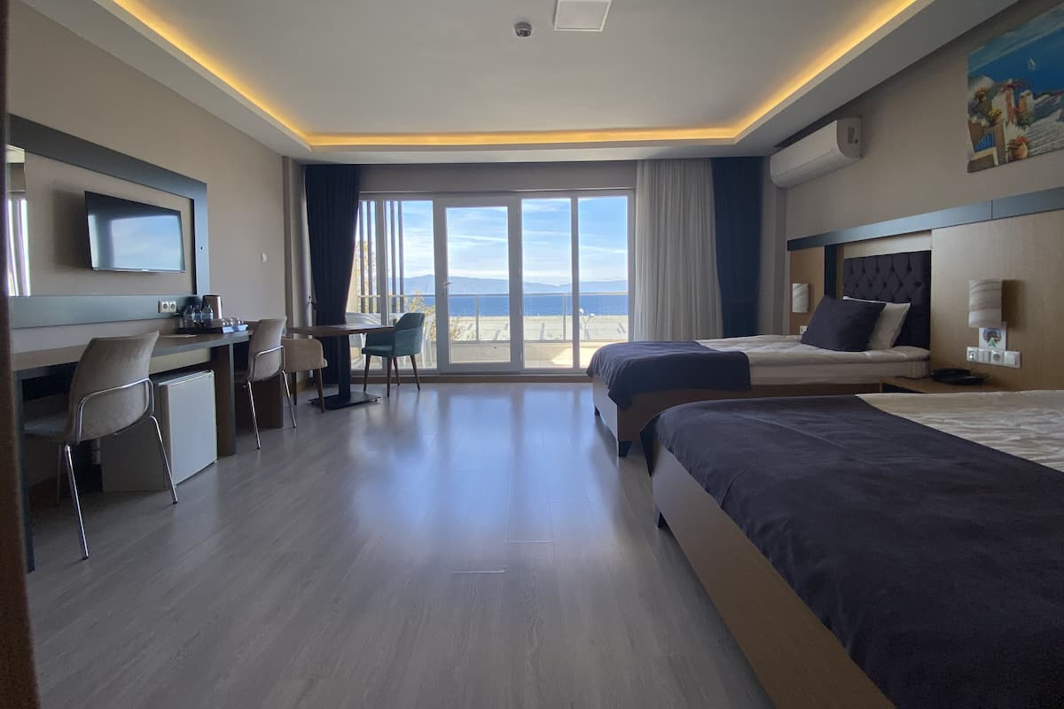 A hotel room with a bed, a desk, a chair, a television, and a large window with a view of the sea.