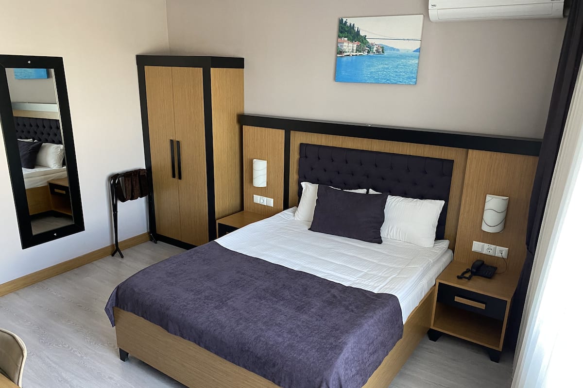 A hotel room with a bed, a wardrobe, a bedside table with a phone, and a wall-mounted lamp.