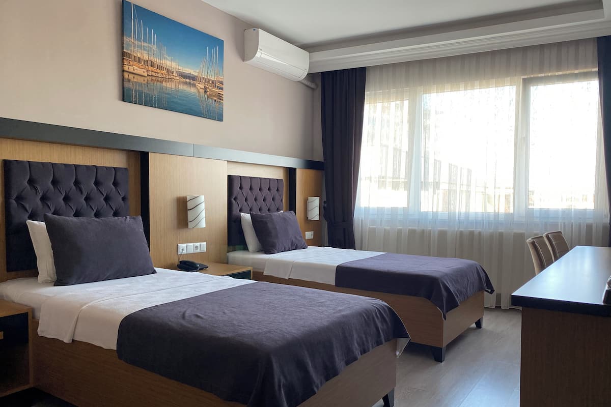 A hotel room with two beds, a desk, and a large window with curtains.