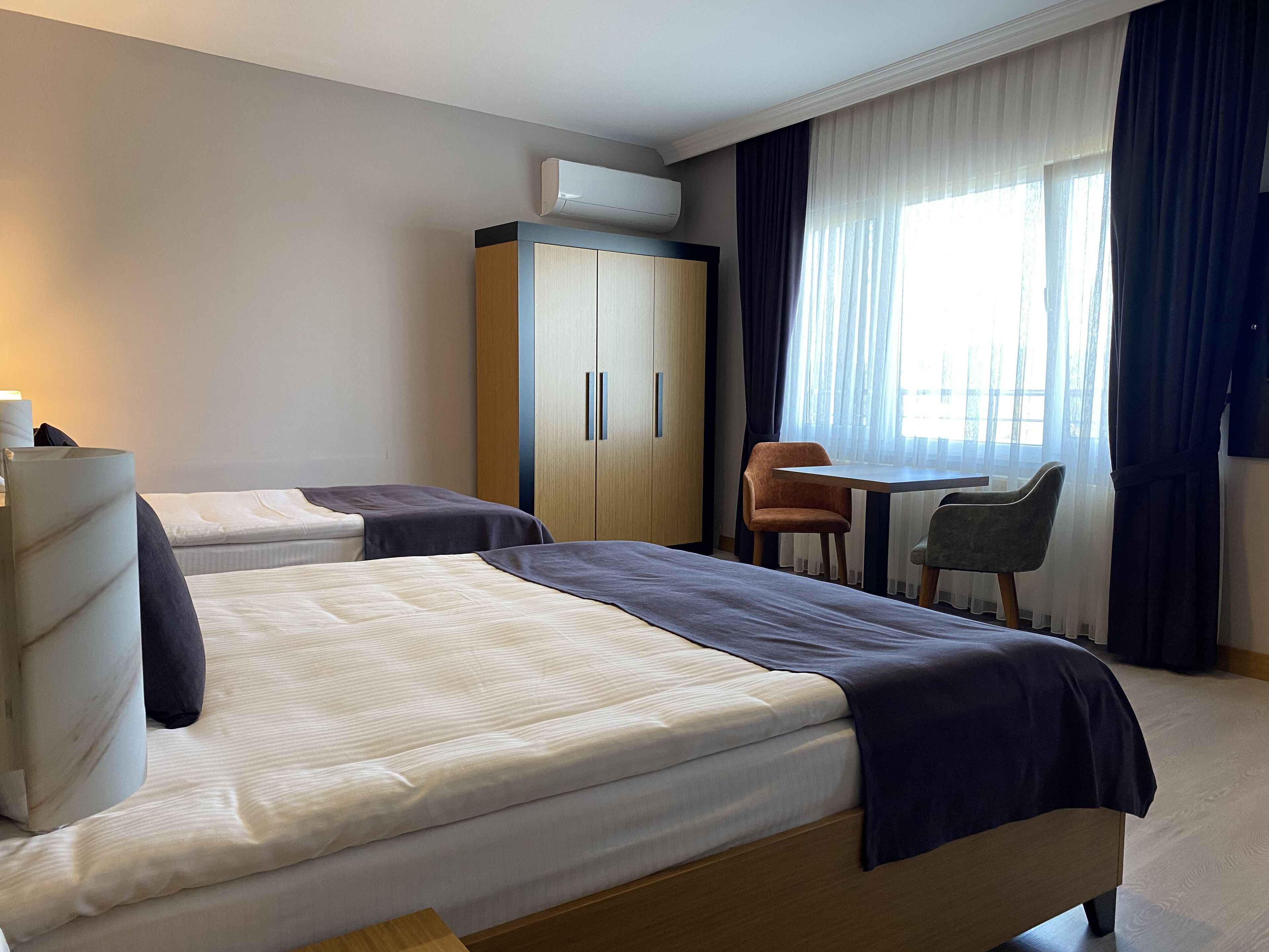 A hotel room with two beds, a desk, and a chair. There is an air conditioning unit above the desk.