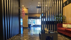 Een moderne lobby met een marmeren vloer, een rode bank en verticale houten lamellen.