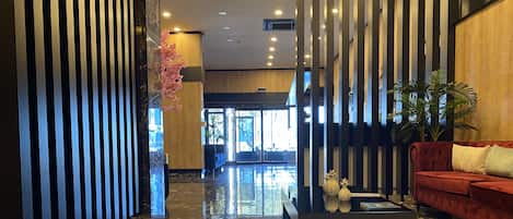 A modern lobby with a marble floor, a red sofa, and vertical wooden slats.