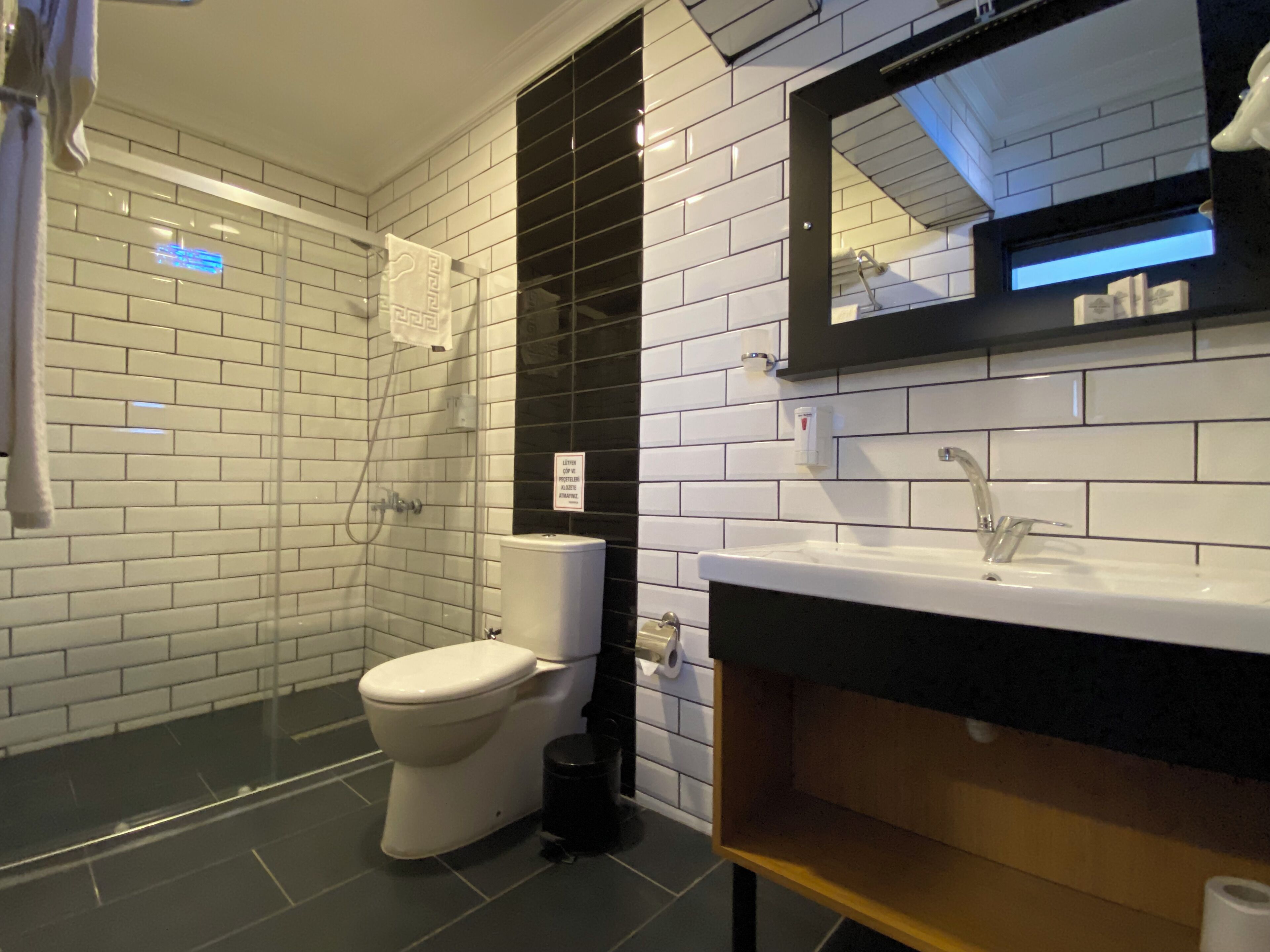 A modern bathroom with white subway tiles, a black and white sink, a toilet, and a shower area.