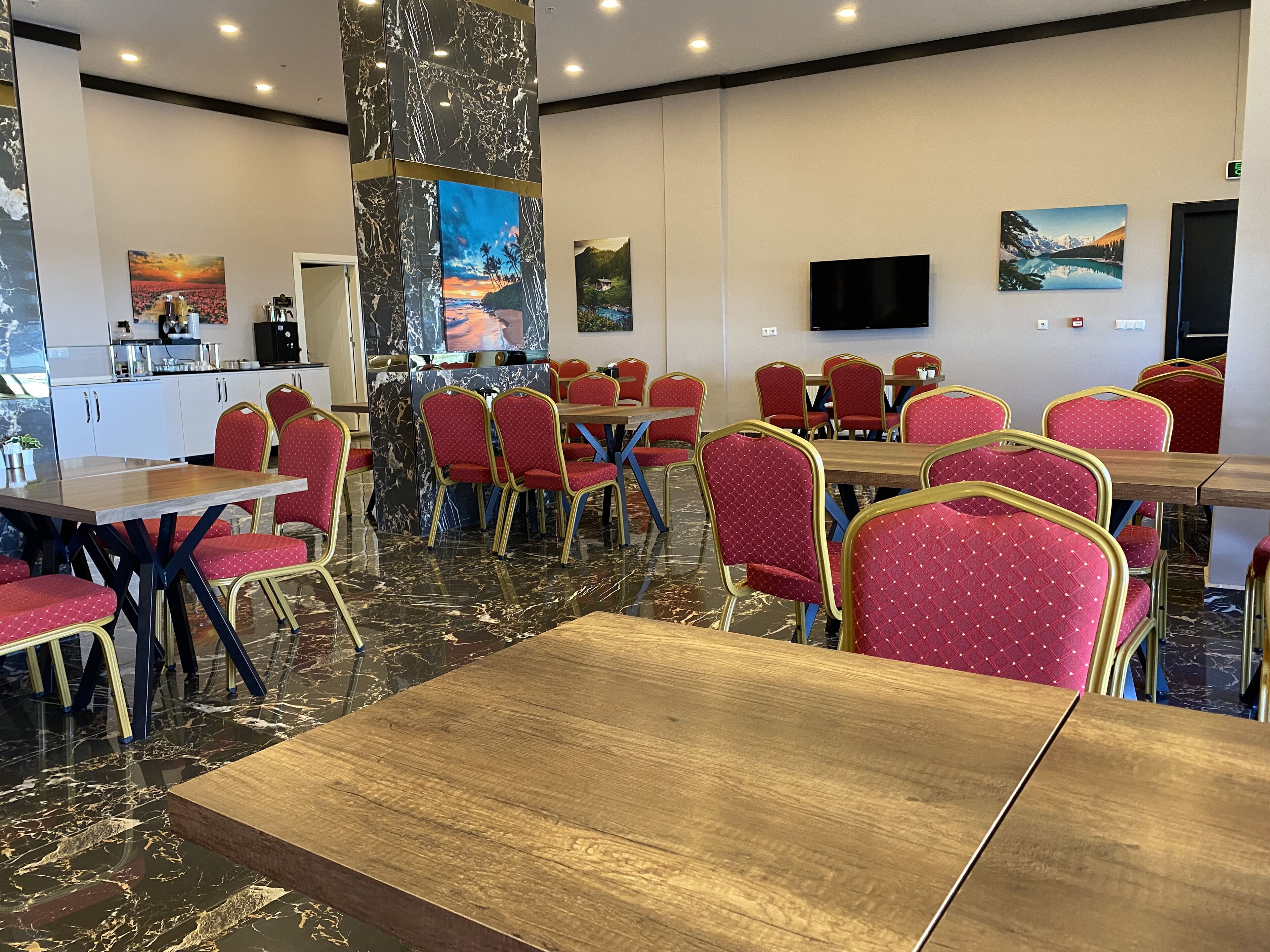 A hotel dining area with marble flooring, red upholstered chairs, and a central pillar with a painting.