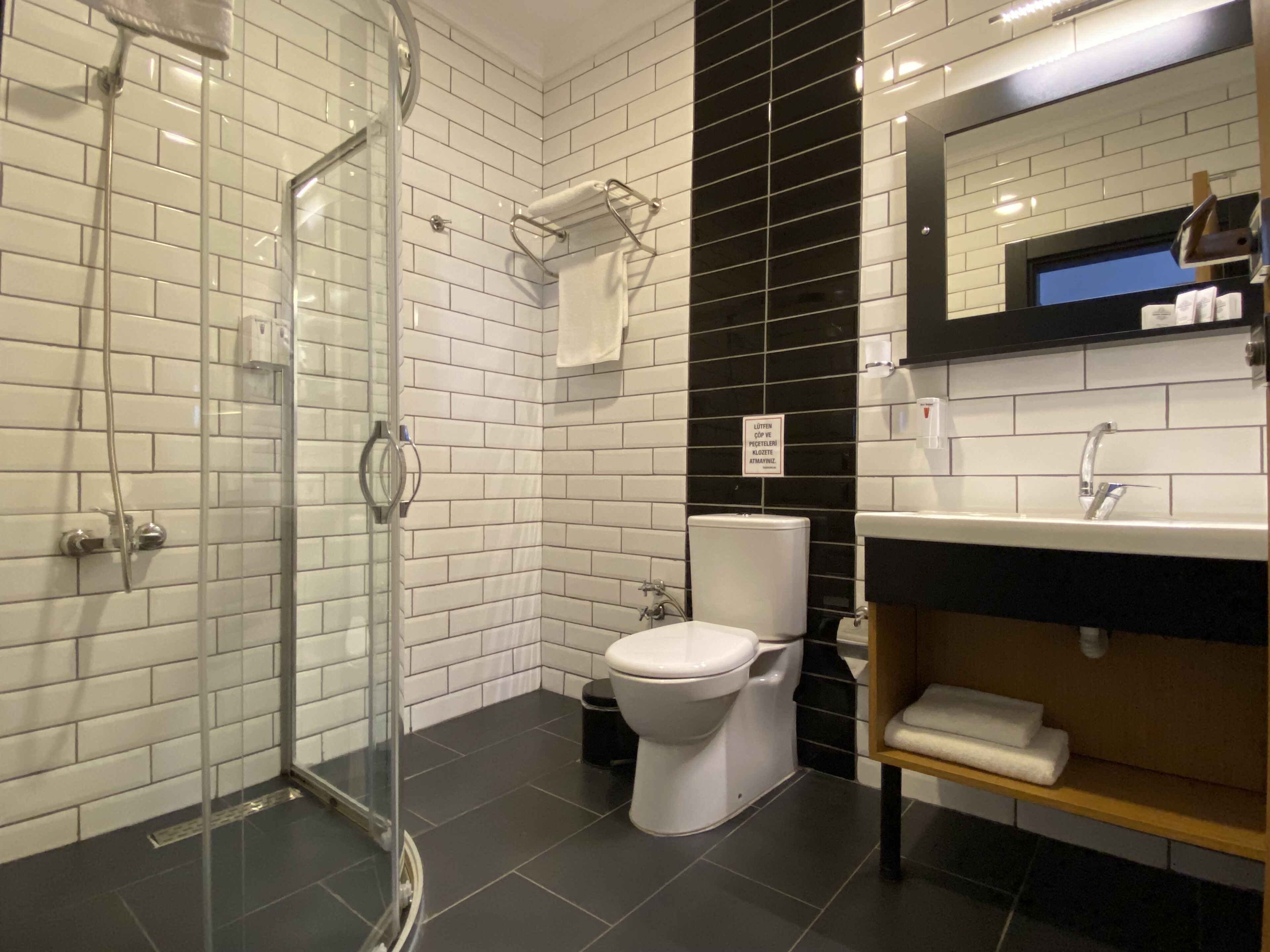 Un baño moderno con cabina de ducha de vidrio, inodoro blanco y pared con azulejos blancos y negros.