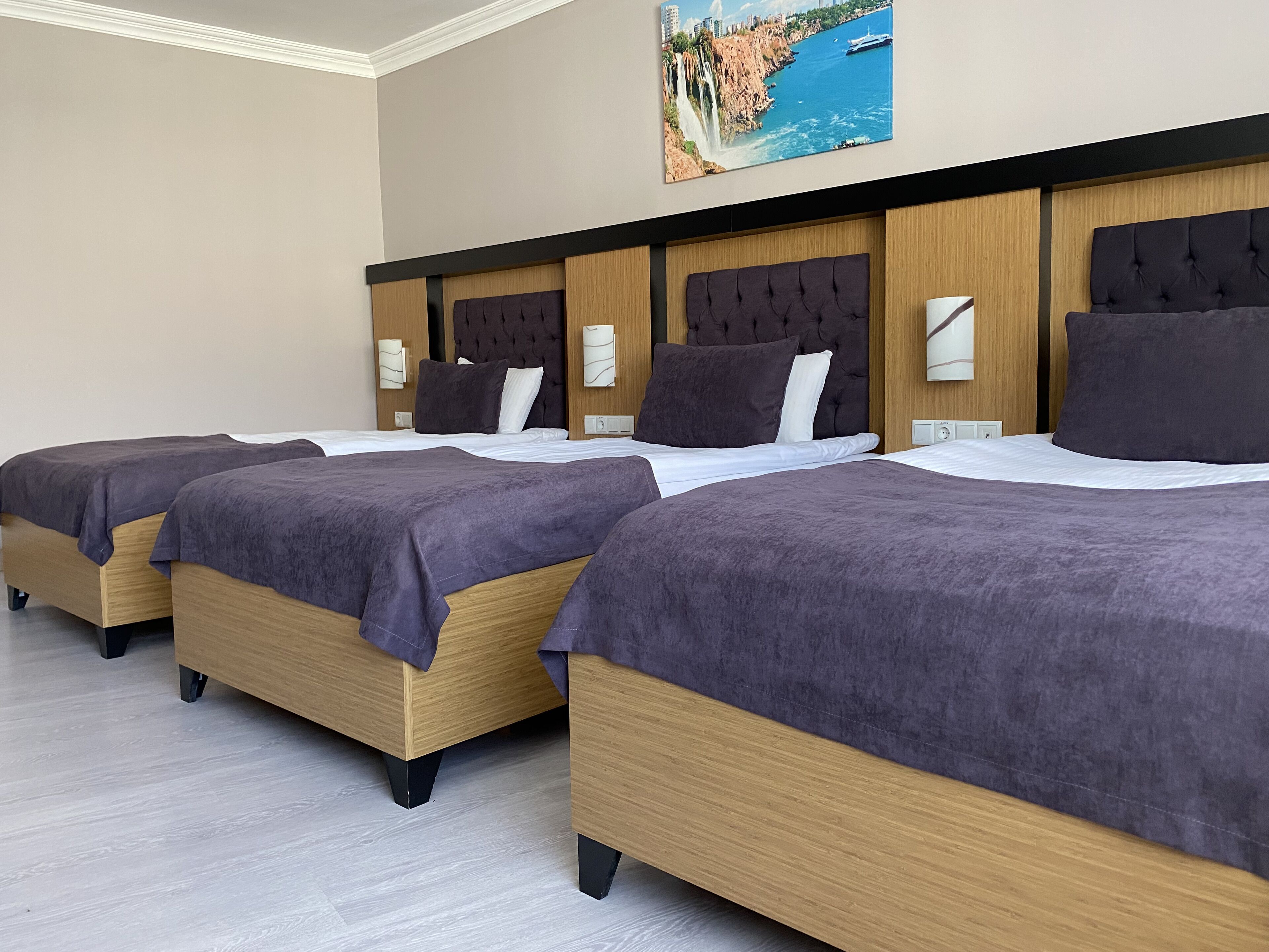 Una habitación de hotel con tres camas, cada una con estructura de madera y cabecero oscuro.